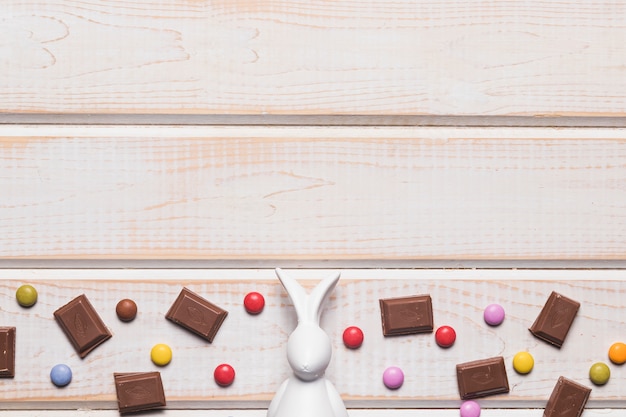 Foto gratuita estatuilla de pascua blanca en medio de trozos de chocolate y caramelos de gema sobre fondo de madera