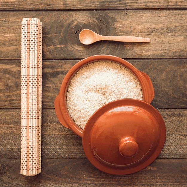 Estera enrollada con arroz en una olla marrón con tapa y cuchara de madera