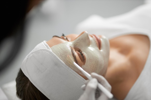 Esteticista aplicando una mascarilla blanca especial en la cara para mujer