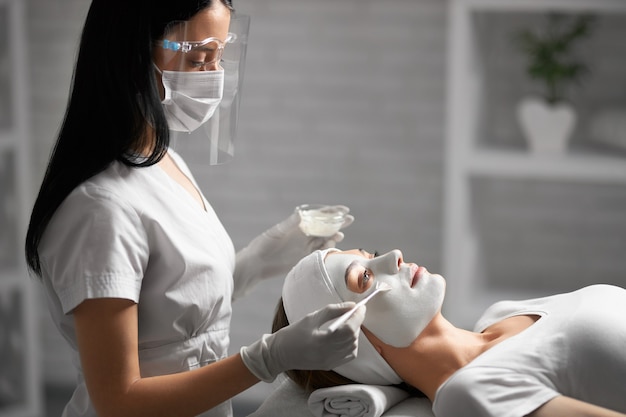 Esteticista haciendo limpieza facial con cosméticos para el paciente.