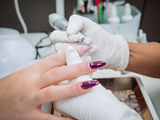 Esteticista profesional usando un taladro de lima de uñas eléctrico para quitar el gel acrílico de las uñas