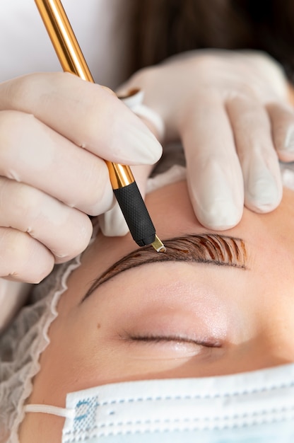 Esteticista realizando un procedimiento de microblading en las cejas de un cliente.