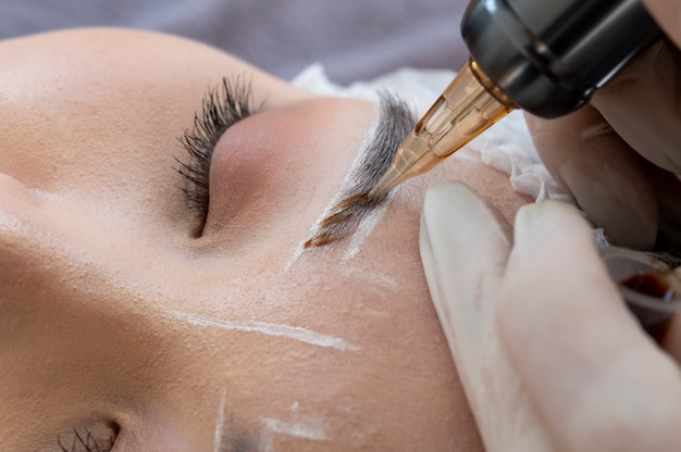 Esteticista realizando un procedimiento de microblading en las cejas de un cliente.