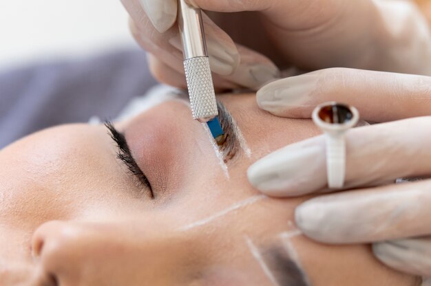 Esteticista realizando un procedimiento de microblading en las cejas de un cliente.