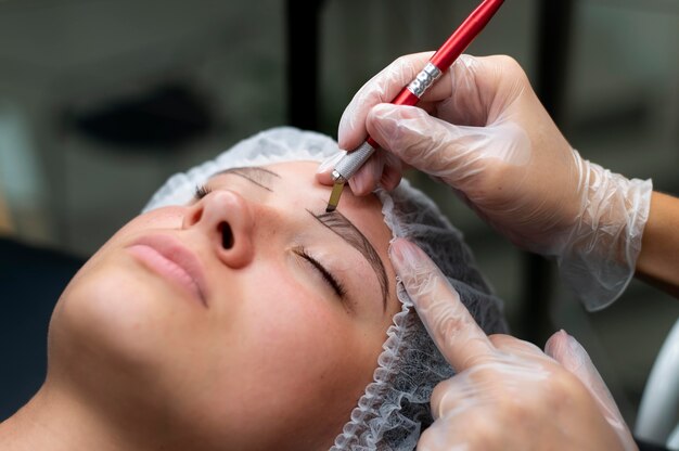 Esteticista realizando un procedimiento de microblading en una mujer joven
