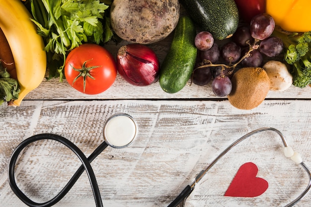 Estetoscopio con forma de corazón cerca de verduras frescas sobre fondo de madera