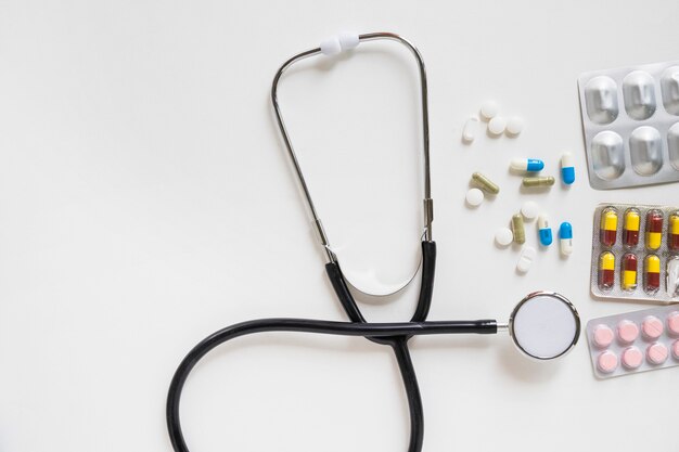 Estetoscopio y pastillas con ampolla de medicina sobre fondo blanco