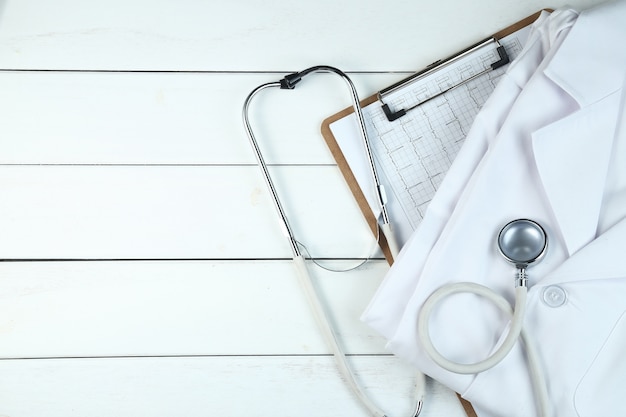 Estetoscopio, sujetapapeles y uniforme médico en blanco escritorio de madera