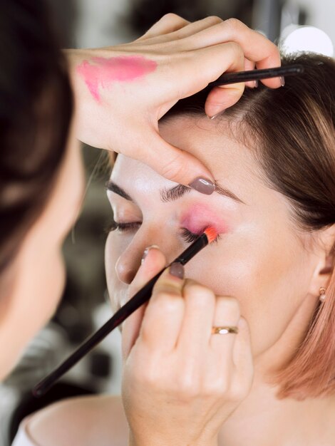 Estilista aplicando sombra de ojos rosa en modelo