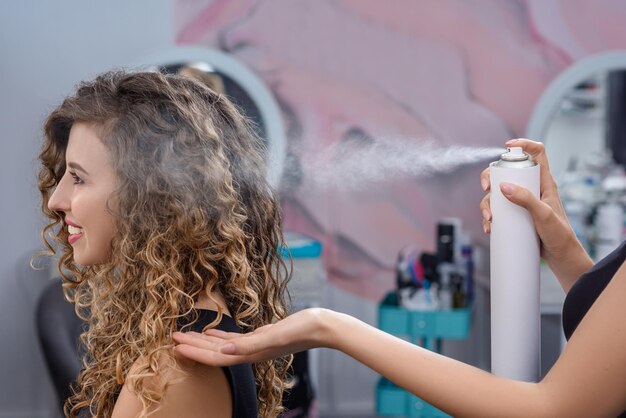 Estilista arreglando el peinado con laca para el cabello en un salón de belleza