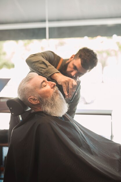 Estilista de cabello recorte de barba a hombre de edad en el salón