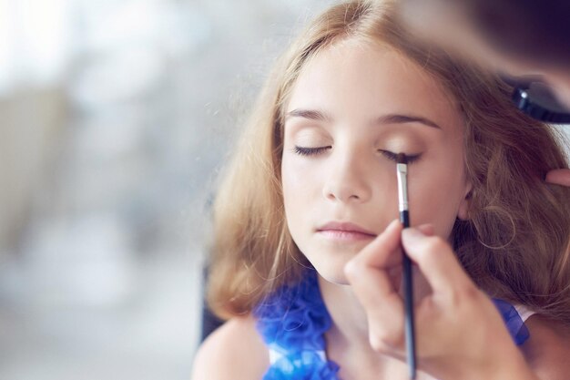 Estilista maquillando a una hermosa modelo de niña. Imagen de primer plano.