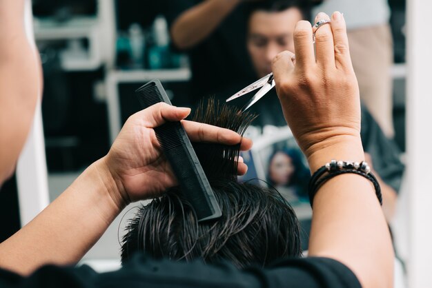 Estilista masculino irreconocible que corta el cabello del cliente frente al espejo