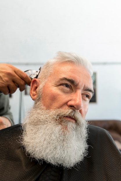 Estilista del pelo que corta el pelo al hombre mayor en peluquería