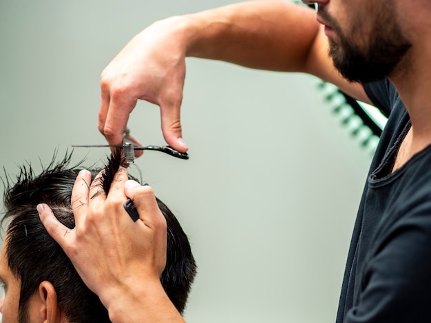 Estilista que corta el cabello del cliente ayudado por tijeras