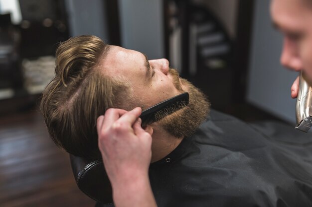 Estilista sin rostro combinándose la barba del hombre