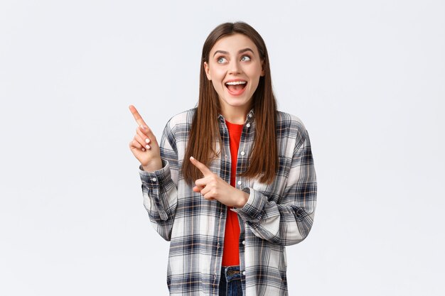 Estilo de vida, diferentes emociones, concepto de actividades de ocio. Mujer feliz emocionada en camisa a cuadros señalando con el dedo la esquina superior izquierda y sonriendo divertida, haciendo una elección, encontró lo que buscaba