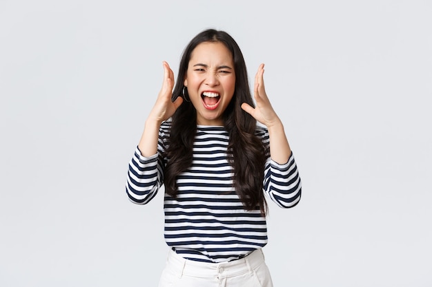 Estilo de vida, emociones de la gente y concepto casual. Loca y angustiada mujer asiática perdiendo los estribos, no puedo soportarlo más, quejándose enloquecida, gritando como teniendo una discusión, dándose la mano agresivamente