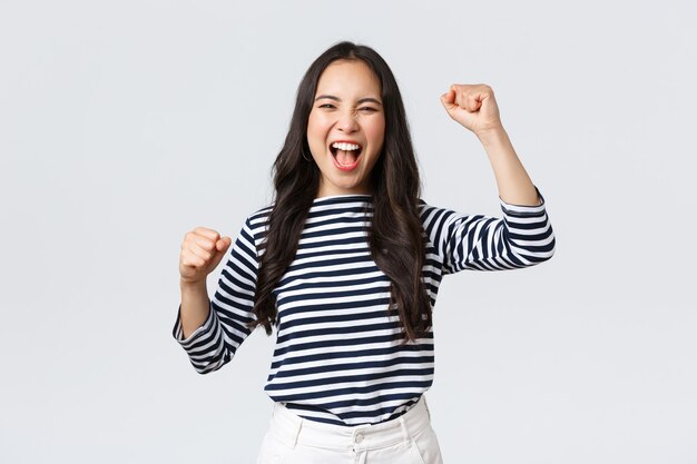 Estilo de vida, emociones de la gente y concepto casual. La mujer asiática feliz y emocionada asiste a la competencia deportiva, animando y cantando para el equipo, levantando las manos y gritando que sí.