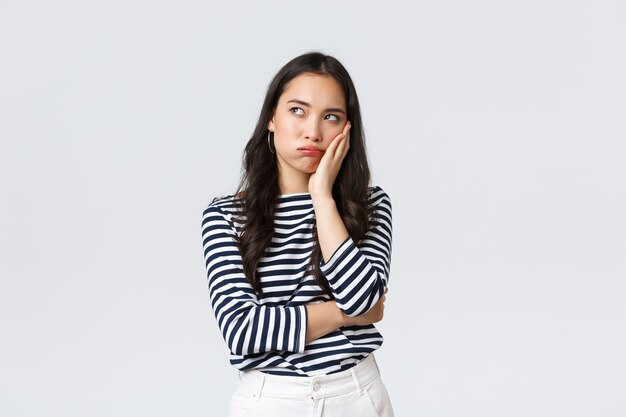 Estilo de vida, emociones de la gente y concepto casual. Mujer asiática reacia molesta de pie aburrida y decepcionada en la fiesta, apoyarse en la palma y mirando hacia arriba, irritada, fondo blanco.