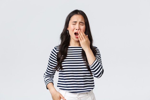 Estilo de vida, emociones de la gente y concepto casual. Mujer cansada soñolienta que trabaja hasta tarde en la oficina, cierra los ojos y bosteza, quiere ir mal. Chica asiática se despertó temprano, necesita café, soporte fondo blanco