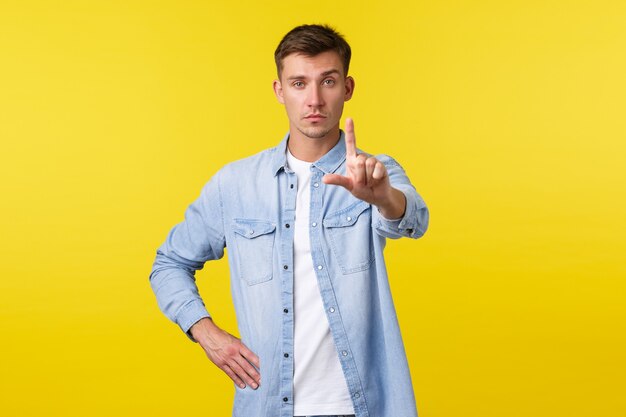 Estilo de vida, emociones de la gente y concepto de ocio de verano. Hombre gay serio con ropa casual, agitando el dedo en señal de prohibición, desaprobar e intentar detener a la persona, dar restricción sobre fondo amarillo.