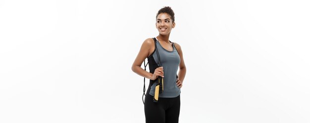 Estilo de vida de entrenamiento deportivo y concepto de fitness retrato de hermosa mujer afroamericana feliz haciendo ejercicio con cuerda de salto aislada en el fondo blanco del estudio