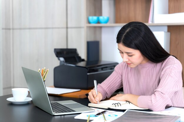 Estilo de vida hermosa mujer de negocios asiática joven usando la computadora portátil en el escritorio de oficina