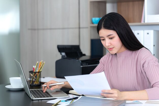 Estilo de vida hermosa mujer de negocios asiática joven usando la computadora portátil y el teléfono inteligente en el escritorio de oficina