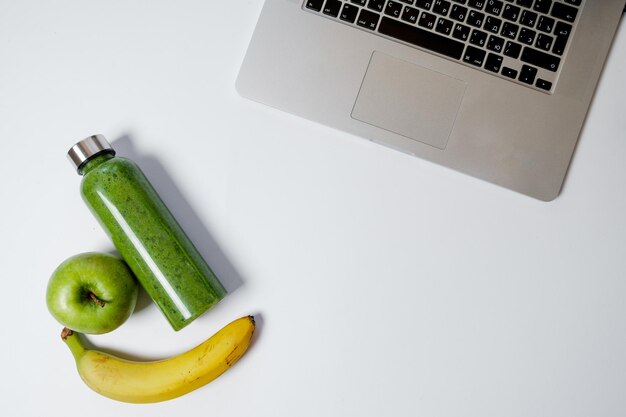 Estilo de vida laboral saludable Laptop con papelería y batidos verdes con manzana en la mesa blanca Vista superior plana