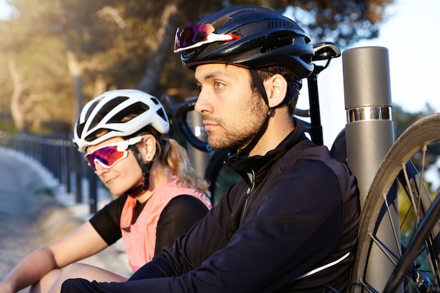 Estilo de vida saludable y activo. Dos ciclistas que descansan en el puente en la mañana después de un largo viaje, enfoque selectivo en un hombre joven y guapo con barba y carismático con expresión positiva pensativa