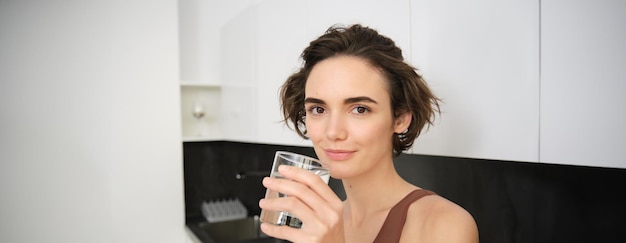 Foto gratuita estilo de vida saludable y bienestar femenino mujer joven y hermosa de pie en la cocina y bebiendo un vaso