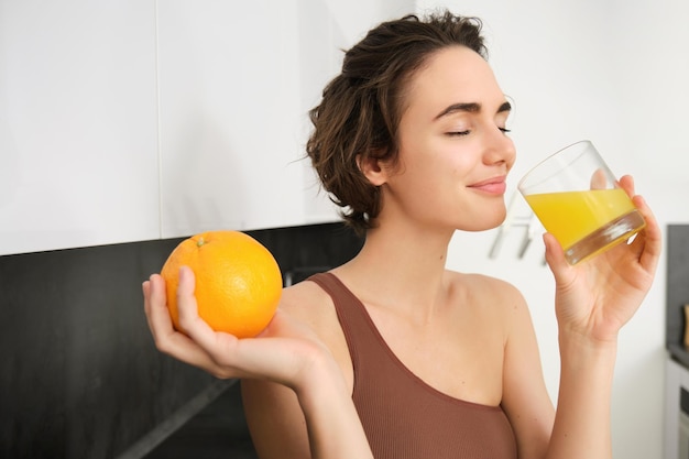 Estilo de vida saludable y deporte hermosa mujer sonriente bebiendo jugo de naranja fresco y sosteniendo fruta en