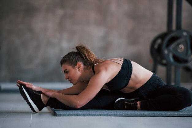 Estírate hacia la pierna derecha. Foto de hermosa mujer rubia en el gimnasio en su fin de semana