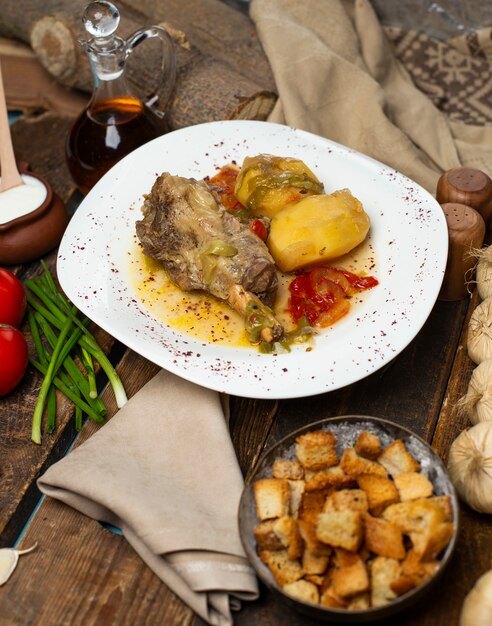 Estofado de carne con papas y caldo aceitoso en plato blanco con galletas de pan.