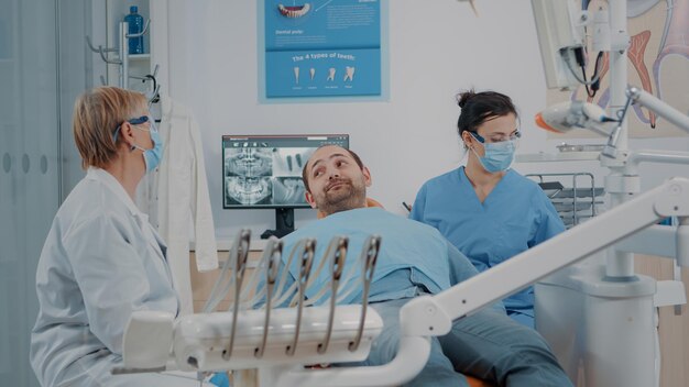 Estomatólogo y enfermera que terminan el procedimiento de cuidado bucal con el paciente en el consultorio de odontología. Dentista dando espejo al hombre para ver los resultados de la dentadura después de la cirugía y el examen dental.