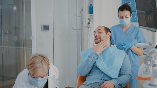 Foto gratuita estomatólogo que consulta al paciente con problemas de caries en el consultorio de odontología, utilizando herramientas e instrumentos dentales. médico y asistente preparándose para el procedimiento quirúrgico con instrumento de perforación.