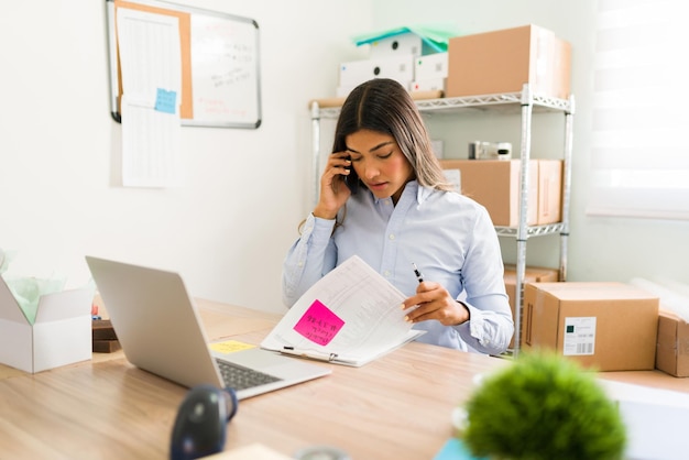 Foto gratuita estoy revisando la información de tu pedido. joven empresaria hablando por teléfono con un cliente antes de enviar un paquete desde su oficina de inicio