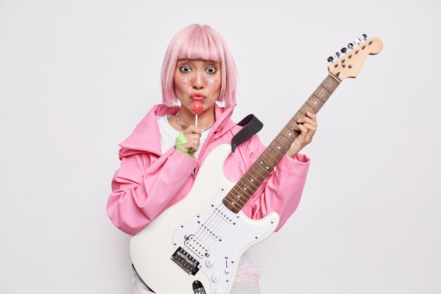 La estrella de rock inspirada tiene el cabello rosado, sostiene una paleta y la guitarra acústica vestida con una chaqueta comparte música con los fanáticos obsesionados por la música y toma lecciones de canto