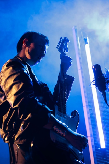 Foto gratuita estrella de rock morena con el pelo corto sosteniendo guitarra eléctrica tocando música rock preparando una canción pesada para actuar en un concierto grunge. mujer guitarrista con chaqueta de cuero ajustando instrumentos eléctricos