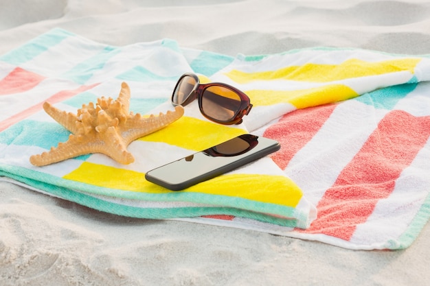 Foto gratuita estrellas de mar, gafas de sol y teléfono móvil mantienen en la playa manta