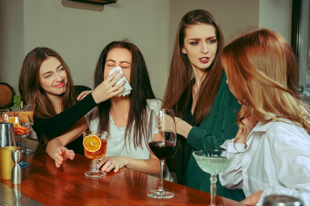 Estrés. Amigas tomando una copa en el bar. Están sentados en una mesa de madera con cócteles. Llevan ropa informal. Amigos consolando y calmando a una niña llorando