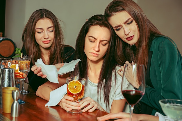 Estrés. Amigas tomando una copa en el bar. Están sentados en una mesa de madera con cócteles.