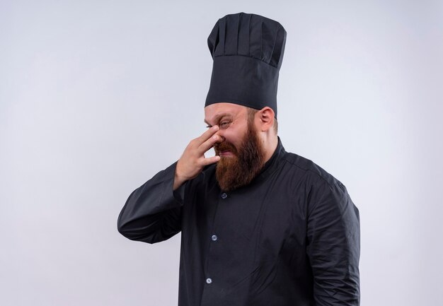 Un estresante chef barbudo en uniforme negro llorando y mostrando negatividad en una pared blanca