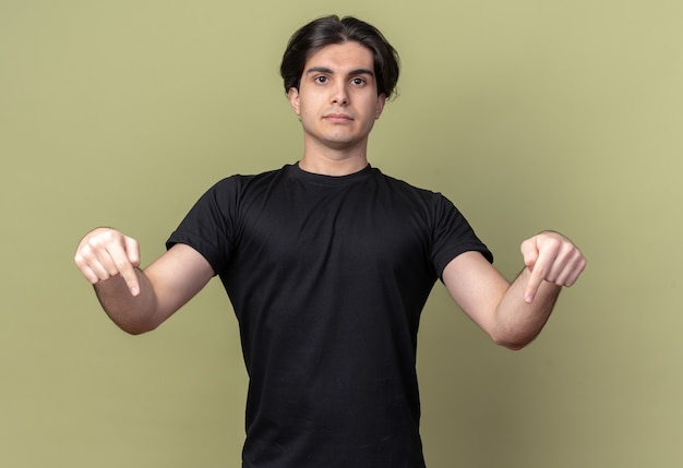 Foto gratuita estricto chico guapo joven con camiseta negra apunta hacia abajo aislado en la pared verde oliva