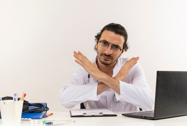 Estricto médico varón joven con gafas médicas vistiendo bata médica con estetoscopio