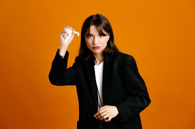 Estricto papel rasgado joven hermosa mujer vistiendo chaqueta negra aislado sobre fondo naranja