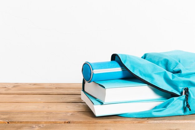 Estuche de libros y lápices azules en la apertura de la mochila en la mesa de madera