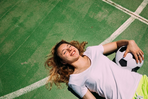 Estudiante adolescente alegre que miente en el campo de fútbol