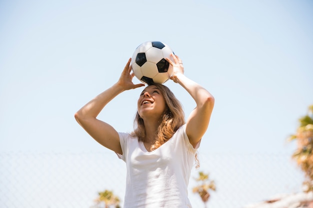 Estudiante adolescente alegre que sostiene el balón de fútbol en la cabeza